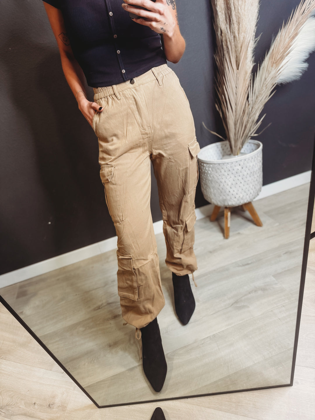 Person wearing beige cargo pants and black shoes standing in front of a mirror.